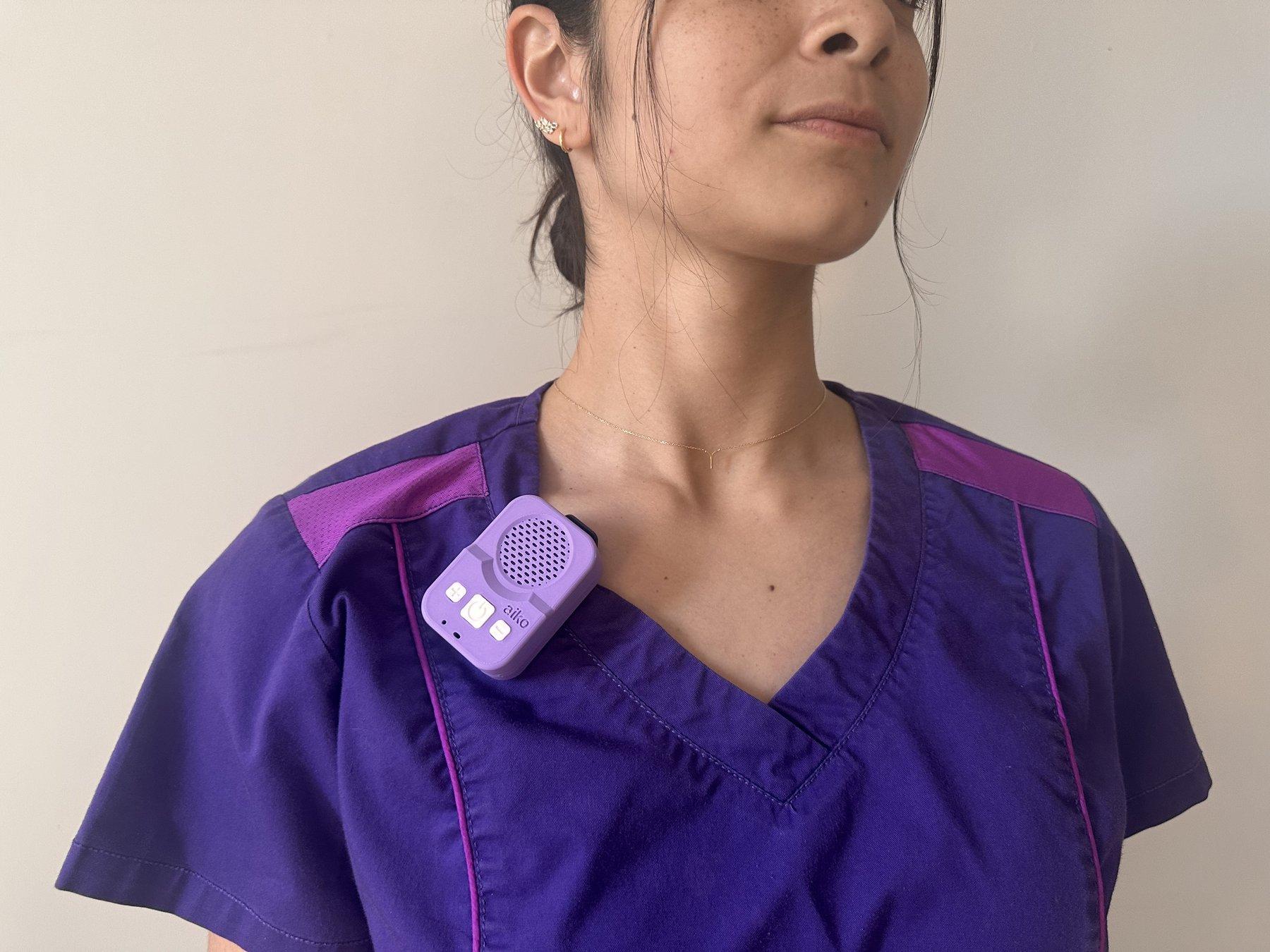 Close-up of a caregiver in purple scrubs with the lavender Aiko device clipped near her shoulder.